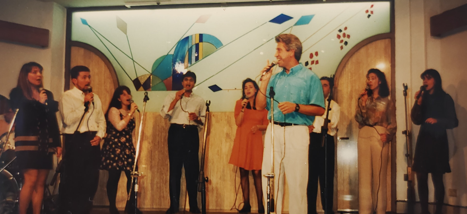 Joan Marc cantando con un grupo de vocalistas ante un mural geométrico en la Església Maragall.