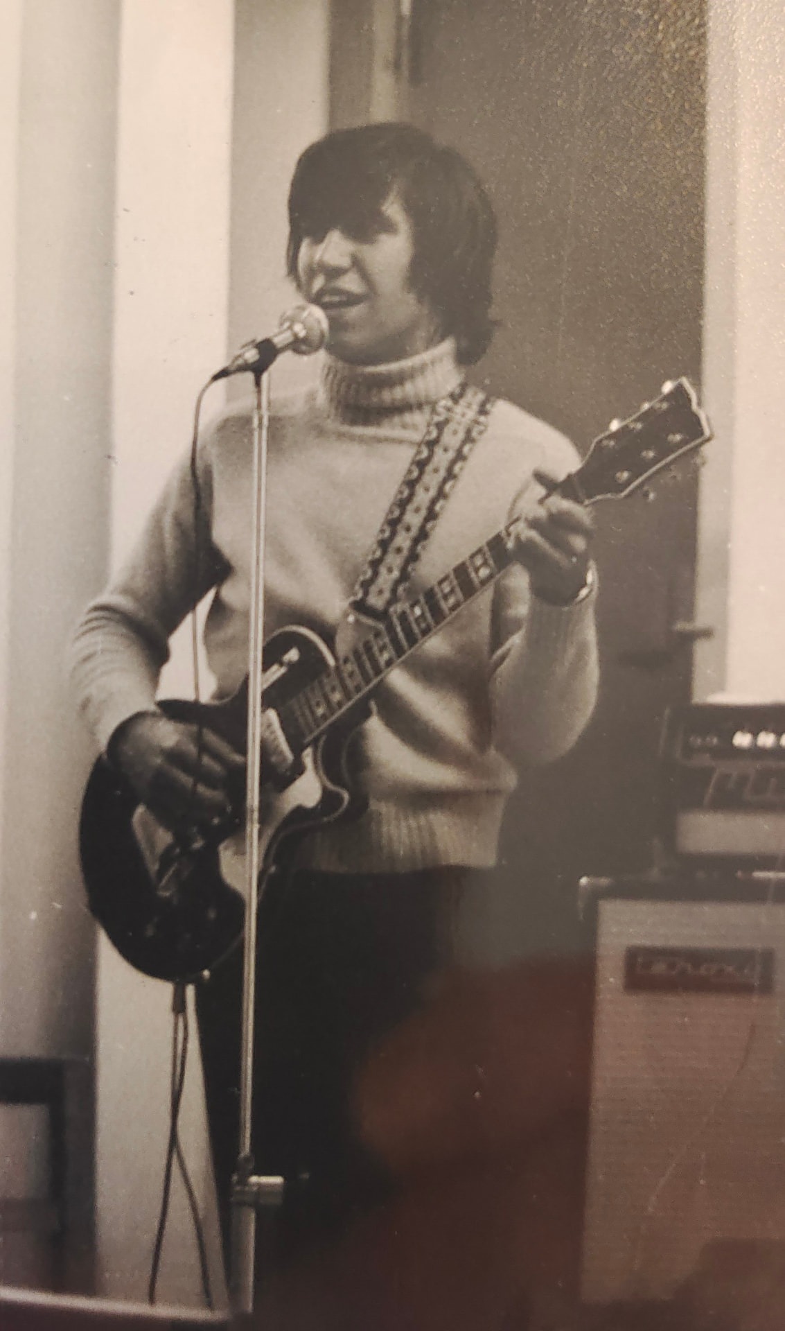 Joan Marc cantando ante un micrófono y tocando la guitarra eléctrica, con un amplificador detrás.