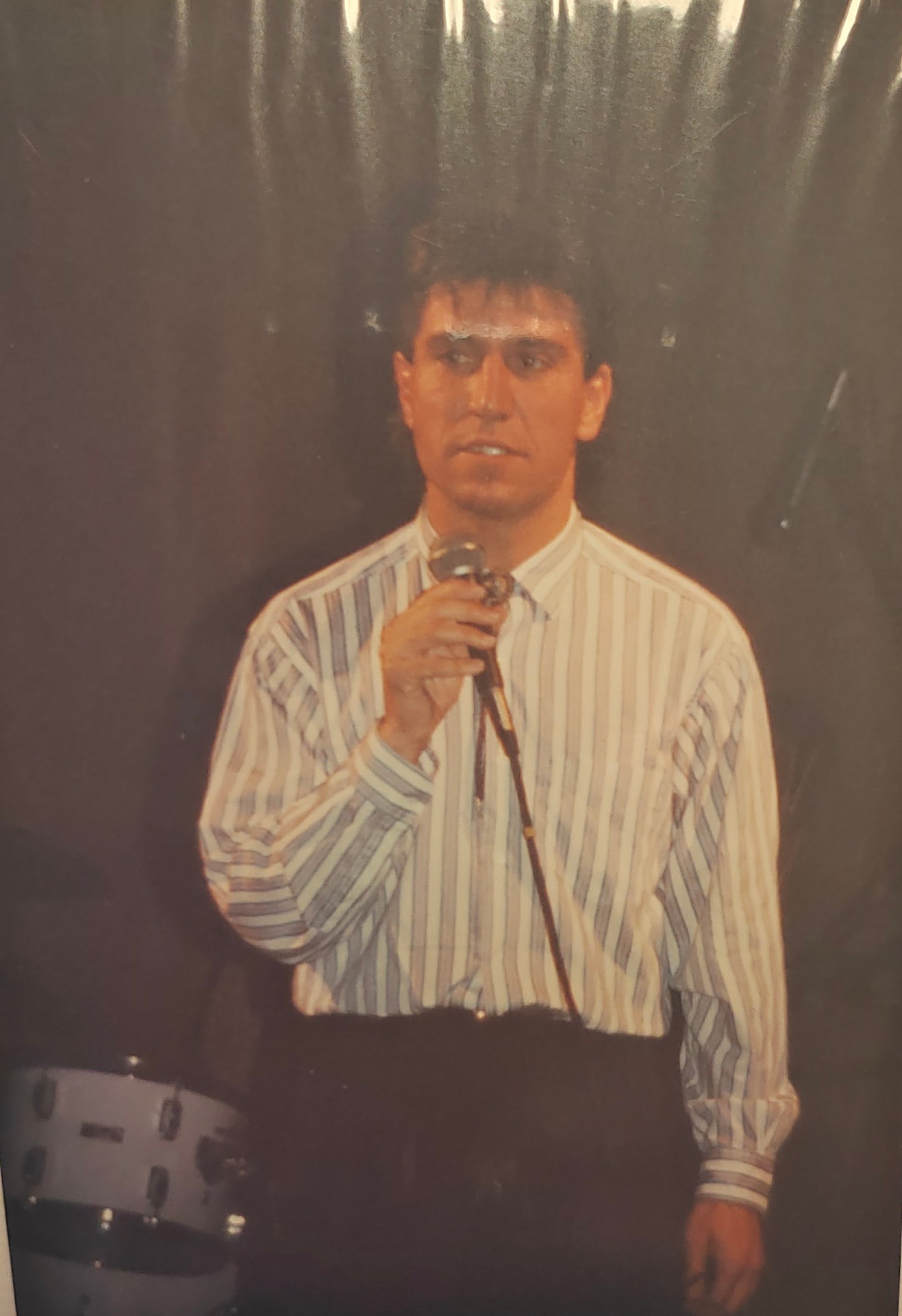 Joan Marc con una camisa de rayas, cantando con un micrófono ante un telón oscuro.