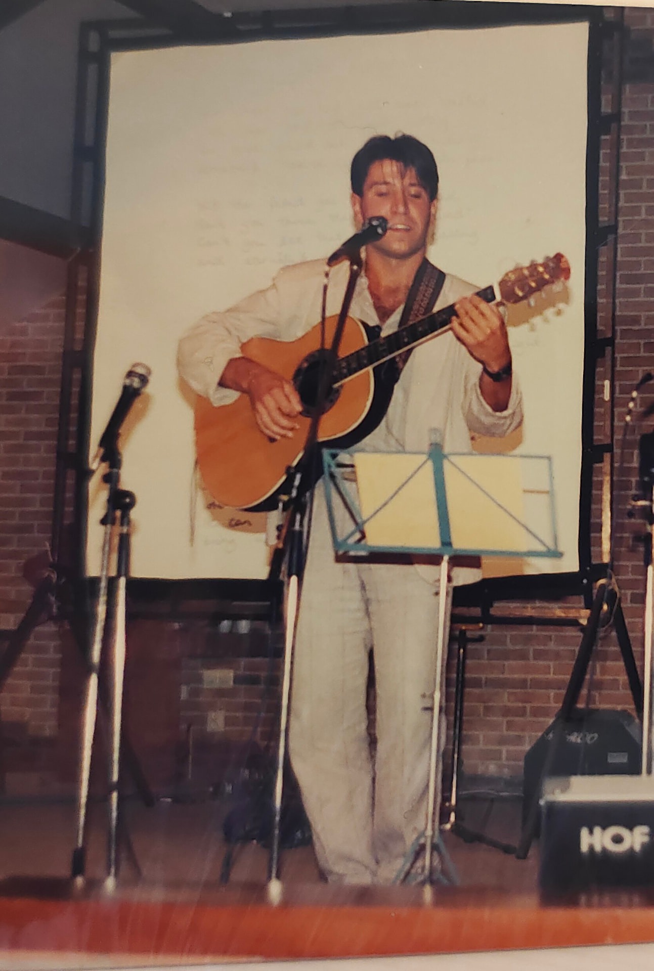 Joan Marc cantando y tocando la guitarra ante un atril y una pantalla clara.