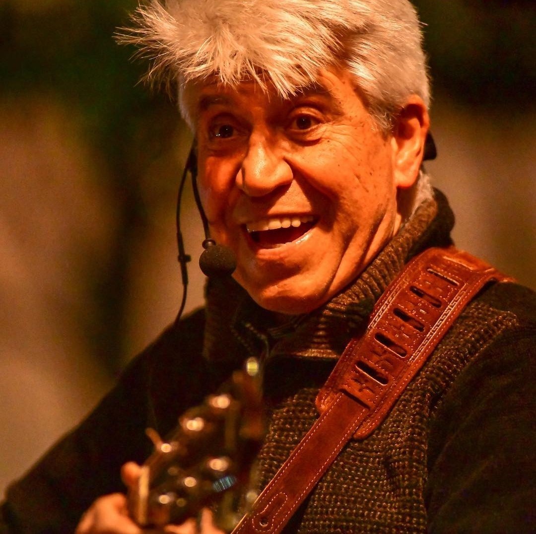 Joan Marc cantando con un micrófono de diadema y la guitarra colgada, en una actuación navideña de luz cálida.