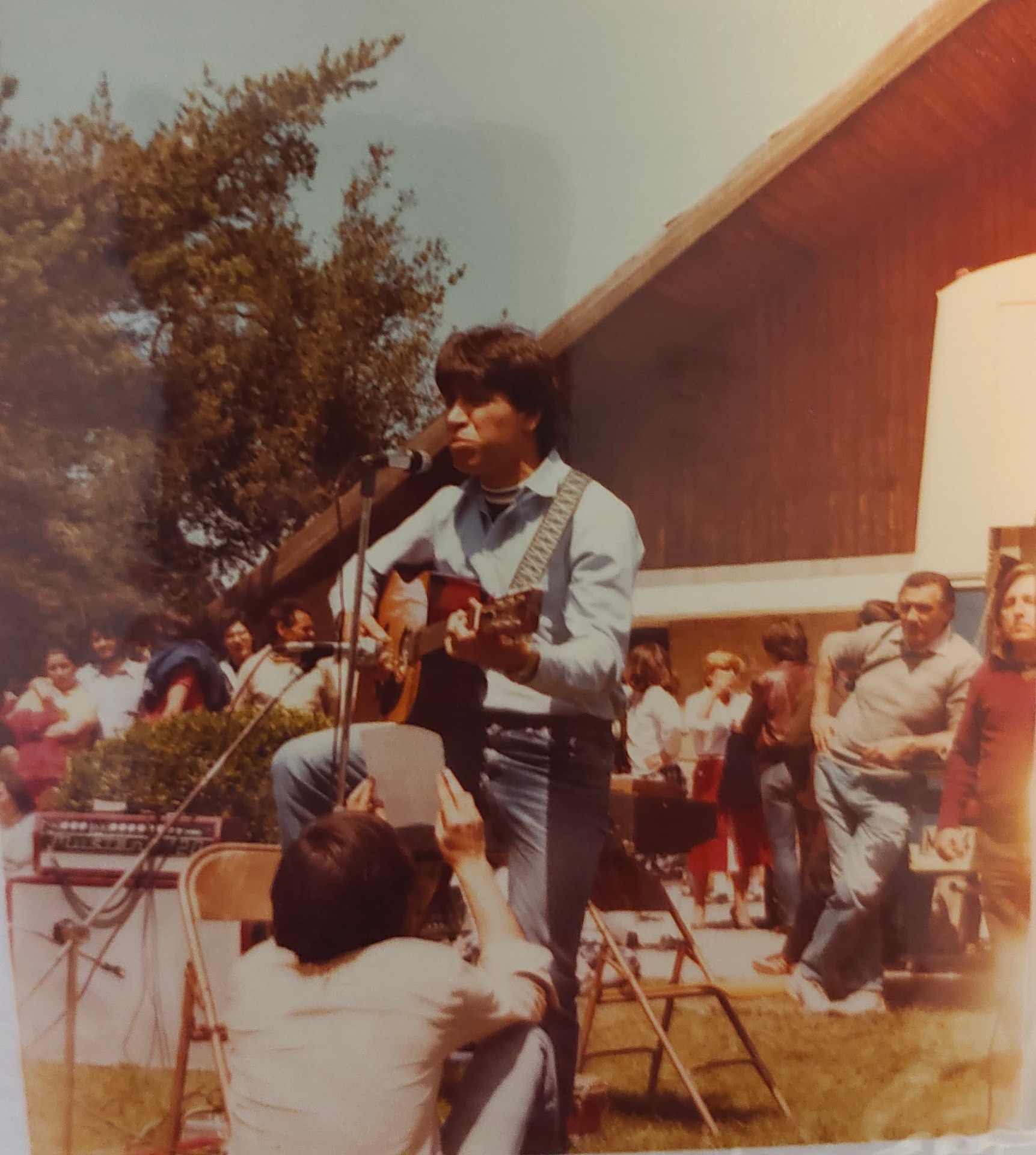 Joan Marc con su guitarra cantando al aire libre frente a un público sentado.