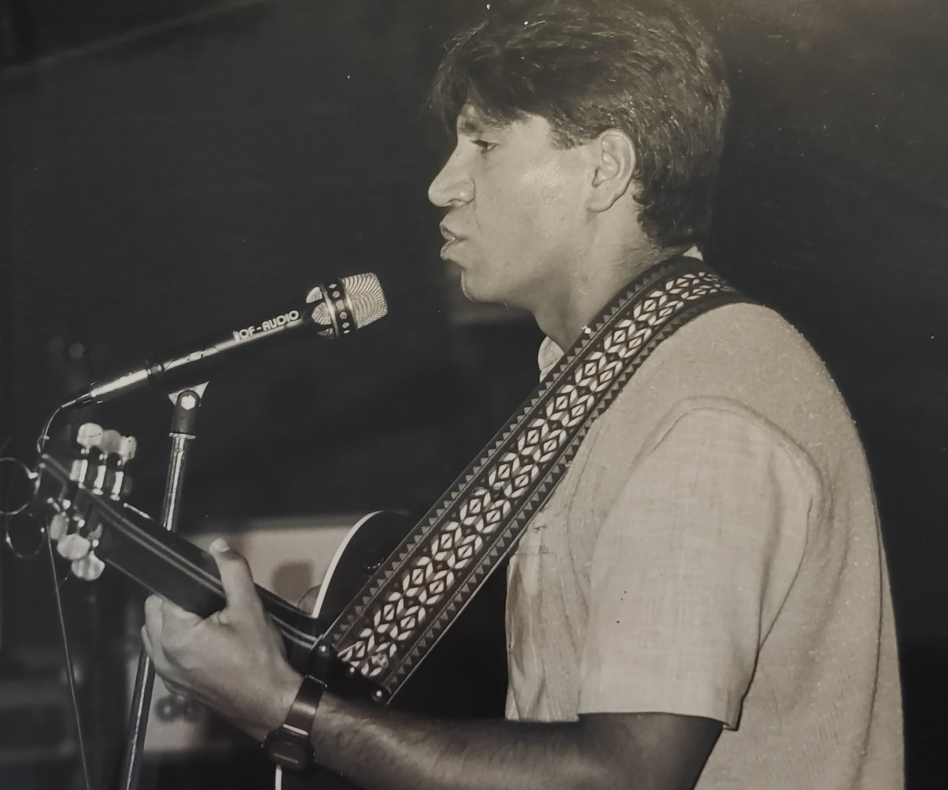 Joan Marc de perfil, cantando y tocando la guitarra ante un micrófono en un escenario interior.