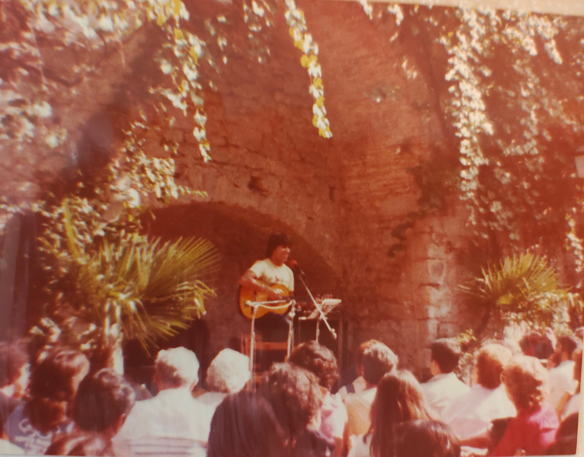 Joan Marc sentado con la guitarra bajo un gran arco de piedra, ante un público que escucha.
