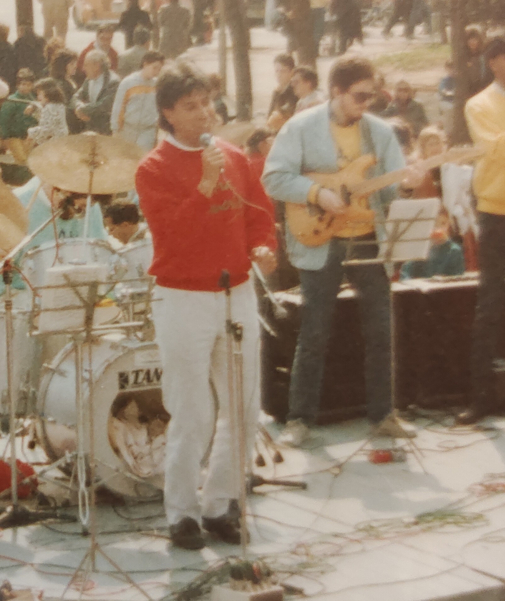 Joan Marc cantando en un escenario al aire libre, con la banda y el público al fondo.