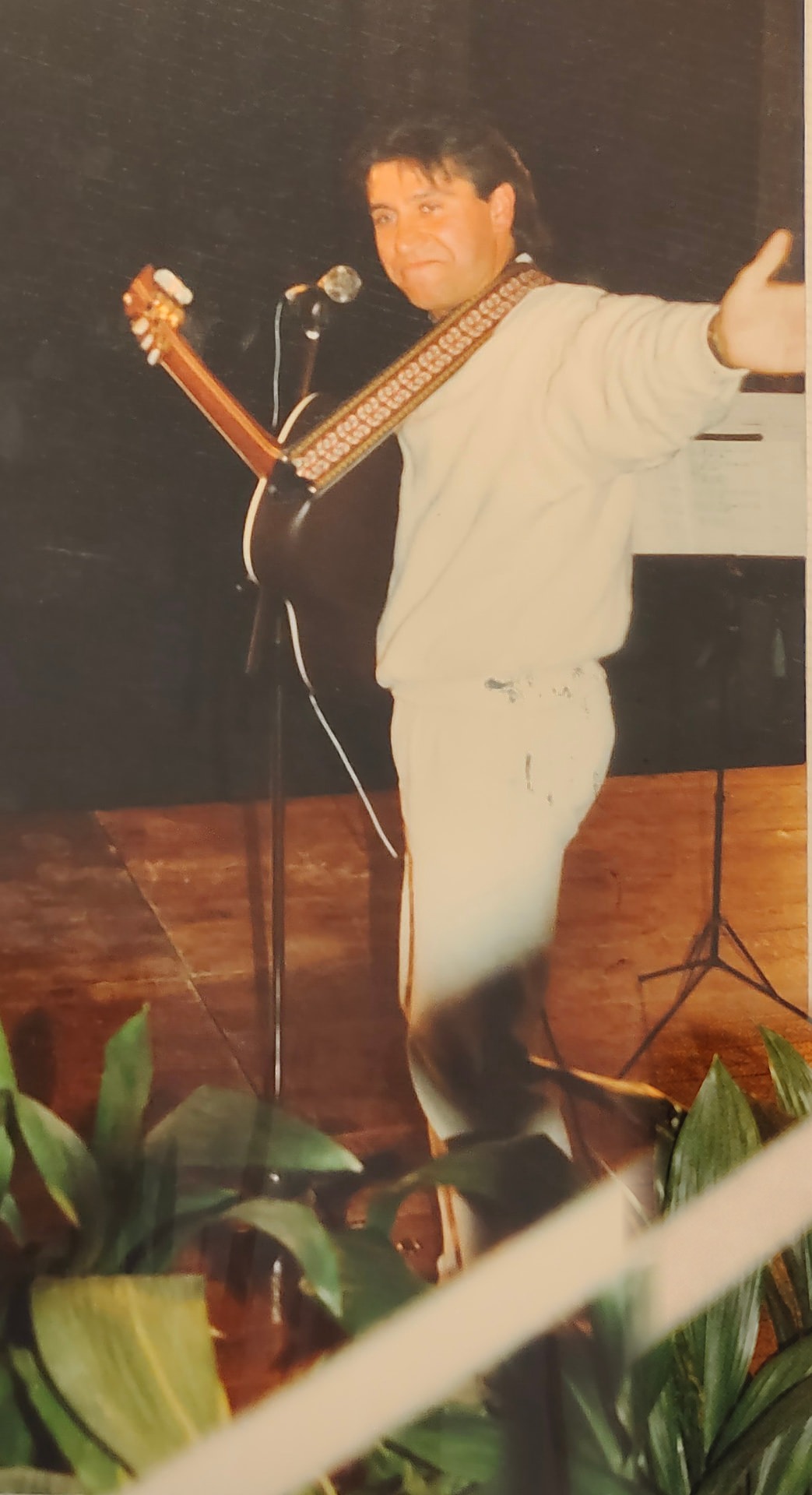 Joan Marc con la guitarra y un brazo extendido en un escenario con plantas delante.