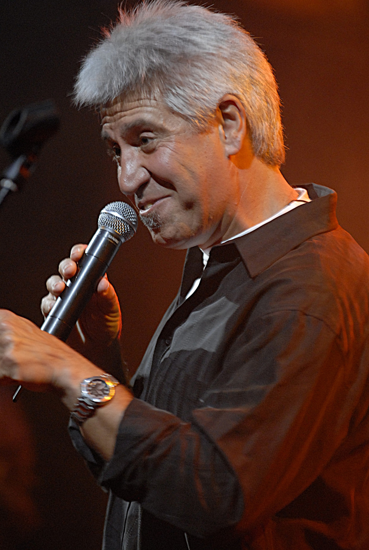 Joan Marc con un micrófono inalámbrico en la mano, hablando al público en un escenario con luz cálida.