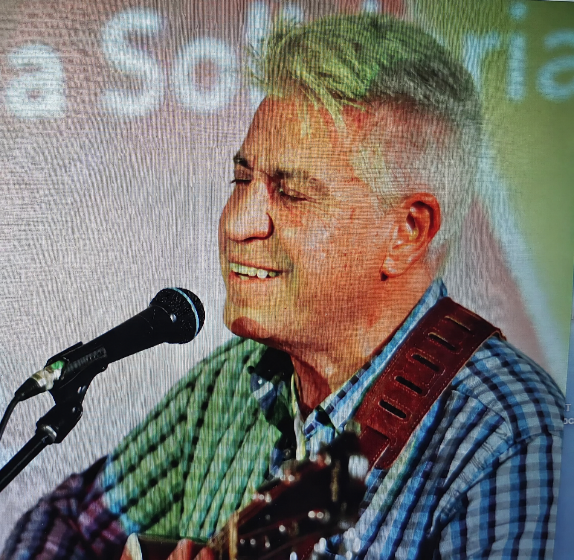 Joan Marc cantando con los ojos cerrados y la guitarra, ante un fondo con el rótulo de la campaña.