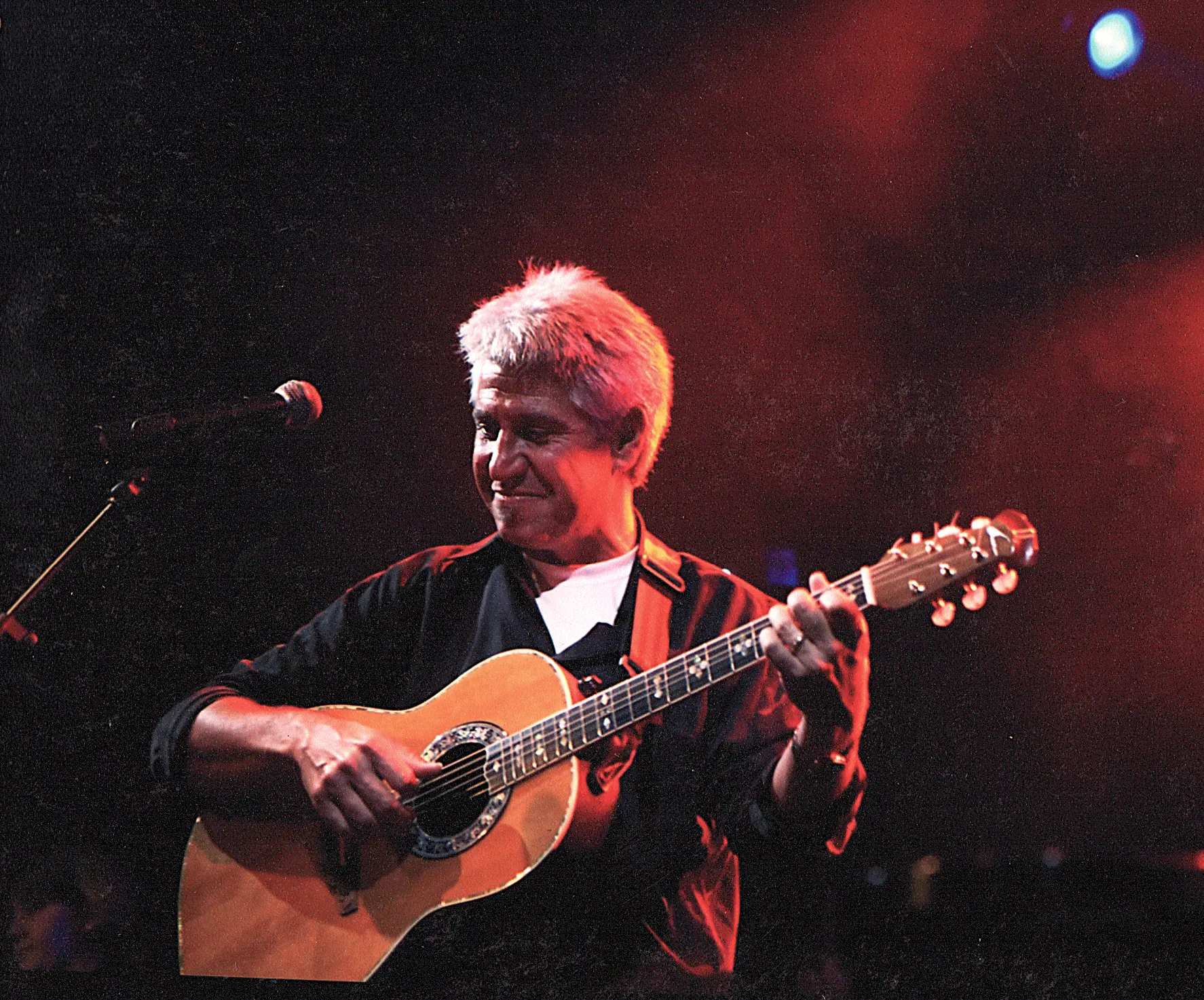 Joan Marc tocando la guitarra y sonriendo, con un haz de luz roja a su espalda.