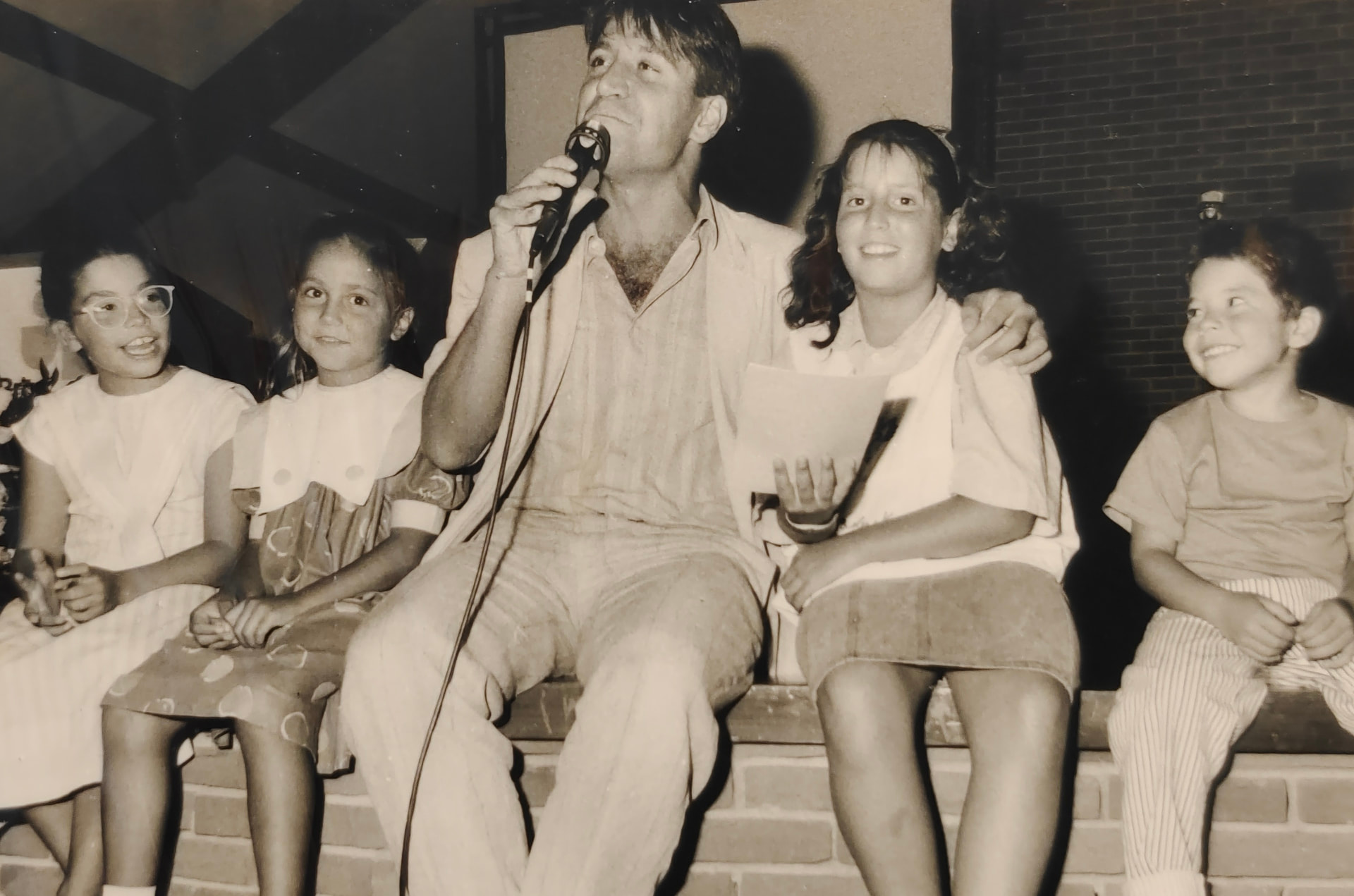 Joan Marc con la guitarra y el micrófono, rodeado de niños sentados a su lado en el escenario.