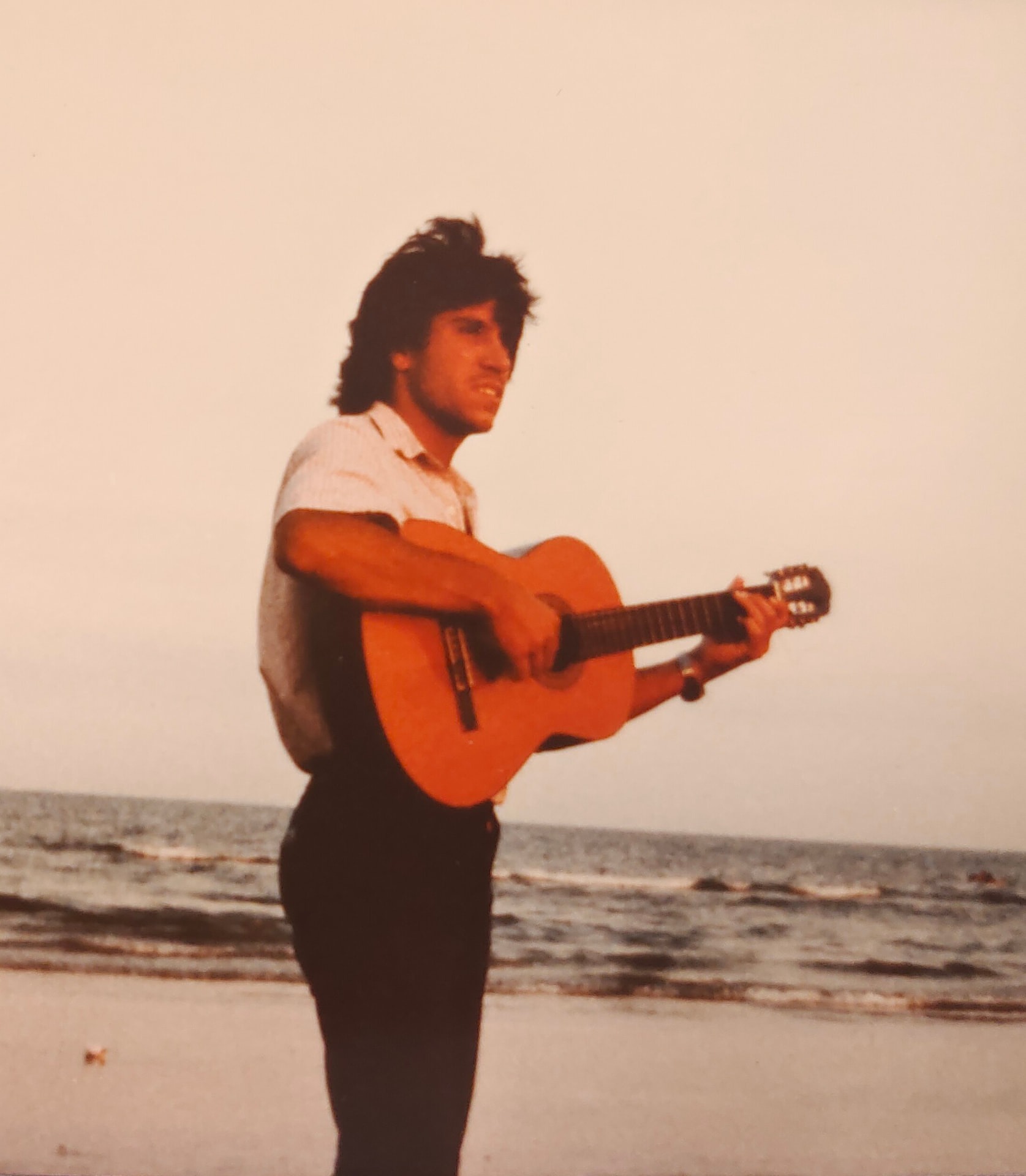 Joan Marc de pie en la orilla de una playa, tocando la guitarra frente al mar.
