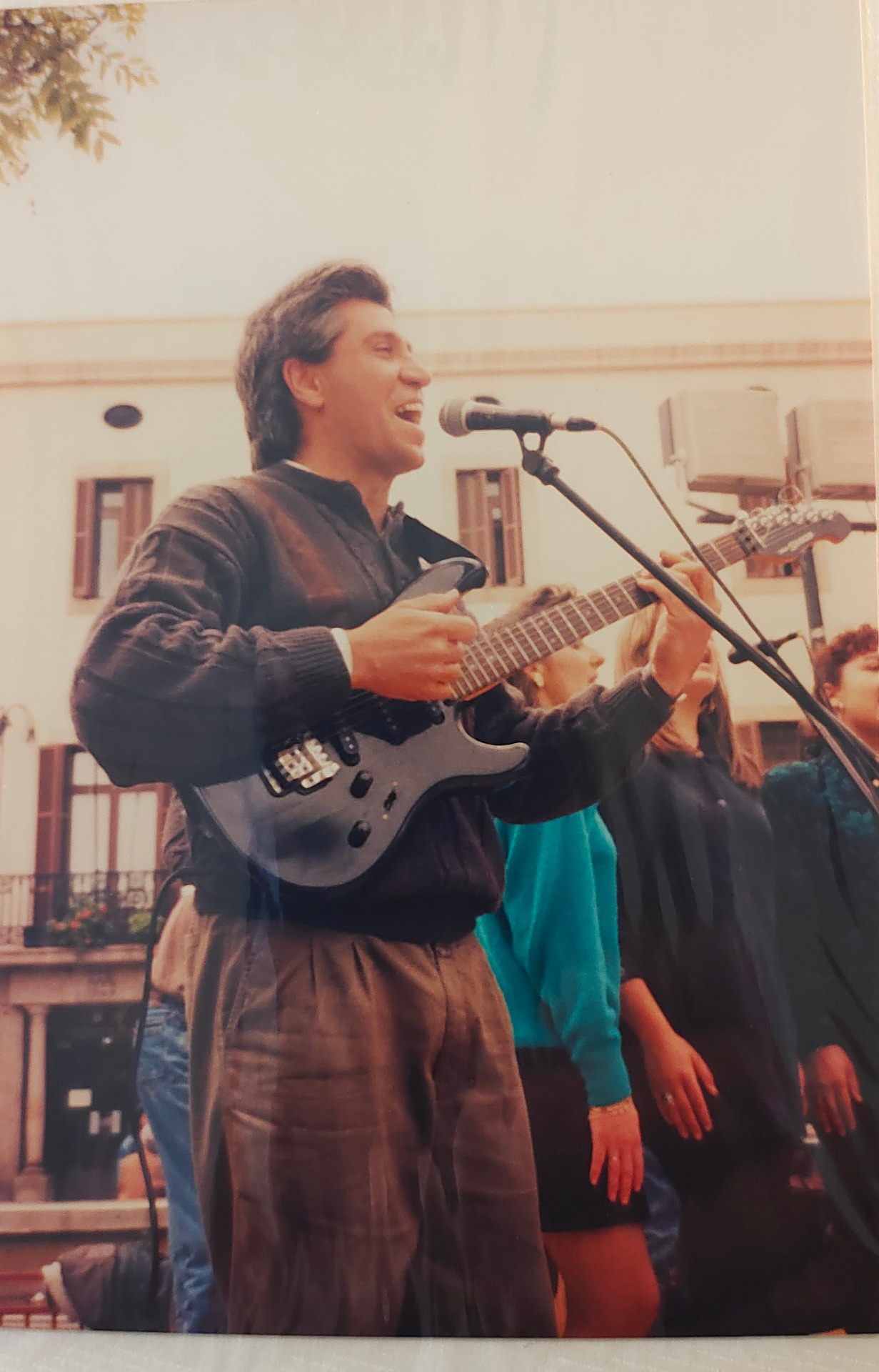 Joan Marc cantando y tocando la guitarra en un interior con músicos detrás.