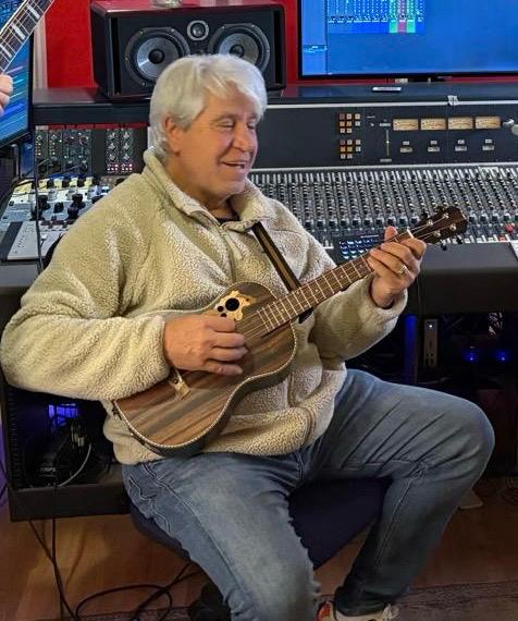 Joan Marc, sentado con un jersey claro, toca un ukelele ante una mesa de mezclas y las pantallas de un estudio de grabación.