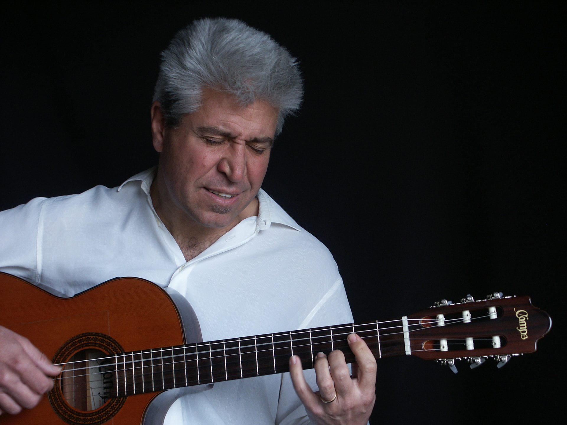 Joan Marc con camisa blanca, mirando el mástil mientras toca la guitarra clásica ante un fondo oscuro.