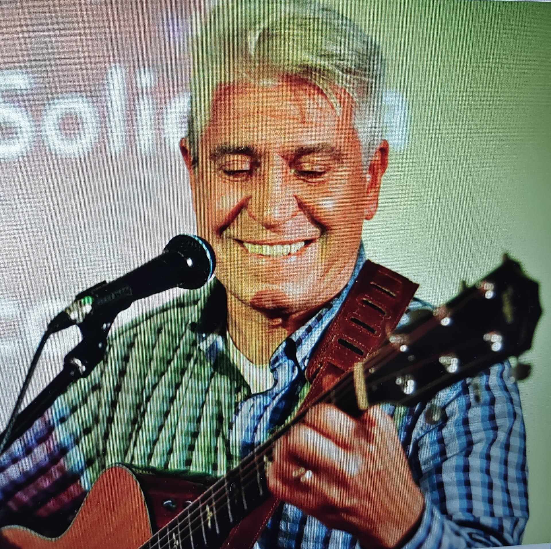 Joan Marc sonriendo ampliamente mientras toca la guitarra ante el micrófono.